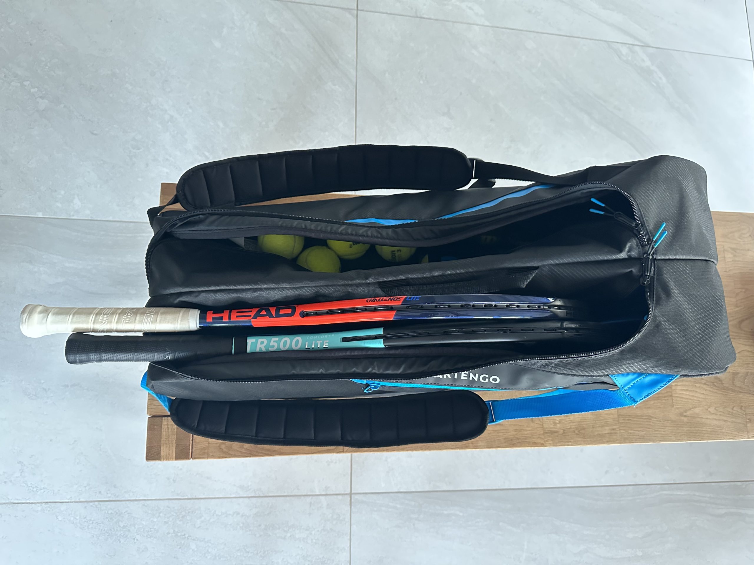 Tennis bag with two rackets and multiple tennis balls, ready for the game.