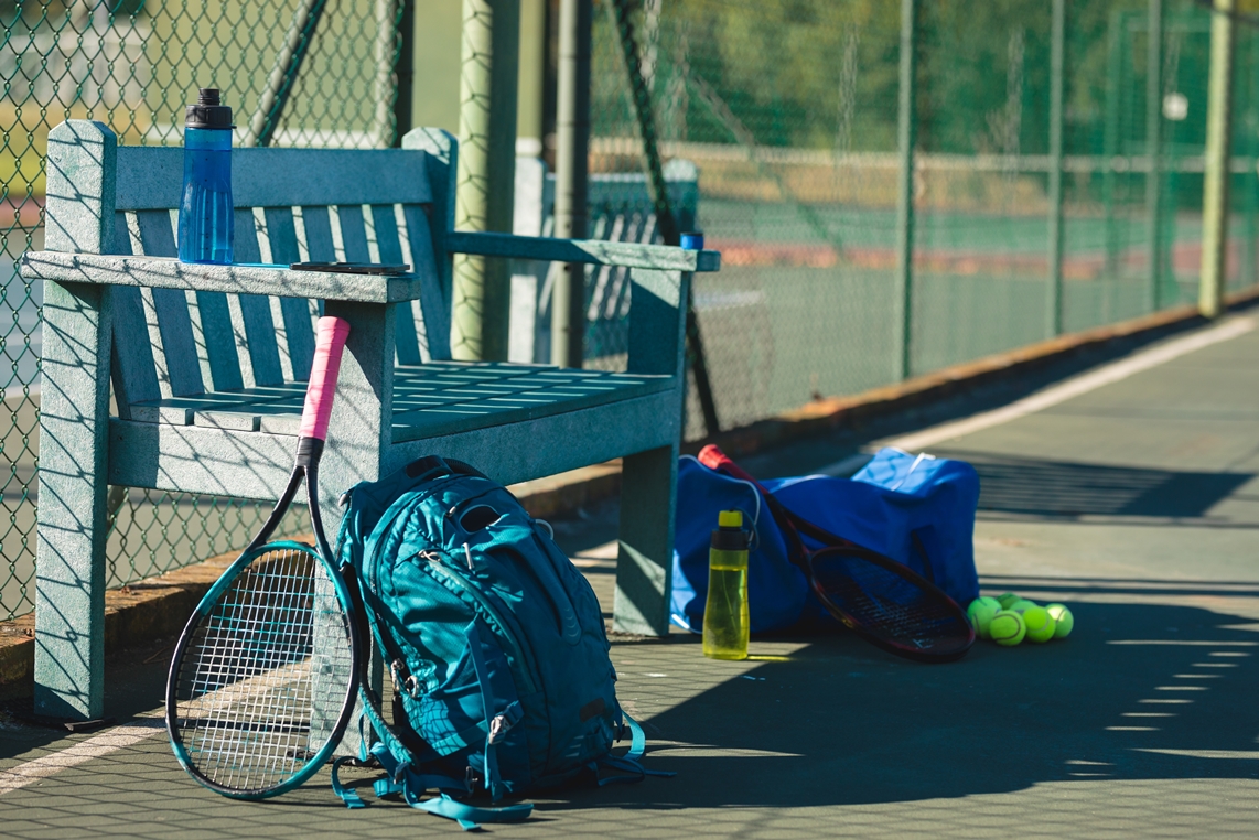 Tennis backpack and bag with assorted equipment including rackets, balls, and gear, arranged for play.